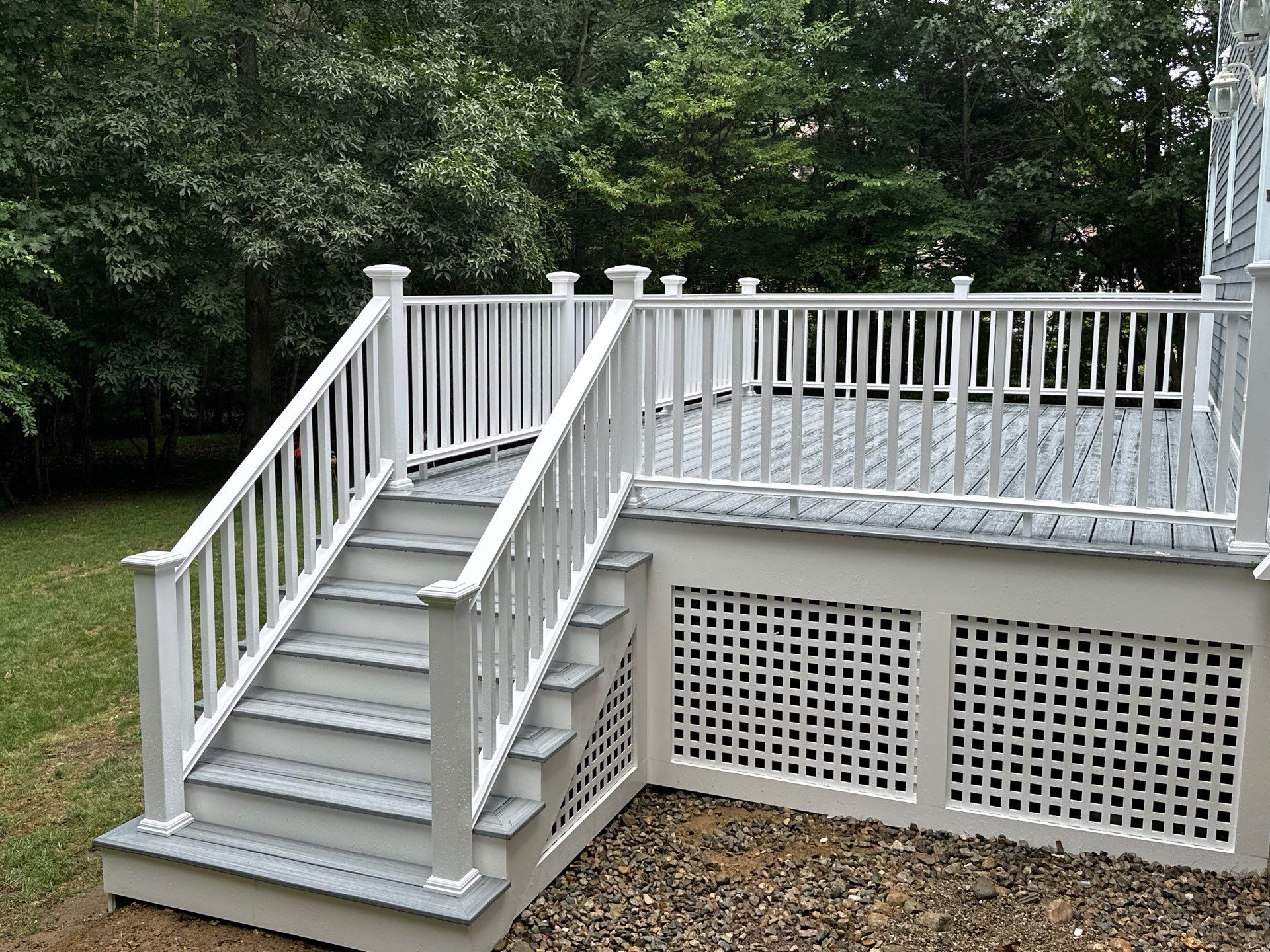 Two-tone grey composite deck with crisp white vinyl railings, wrap stairs, and custom square lattice skirting panels