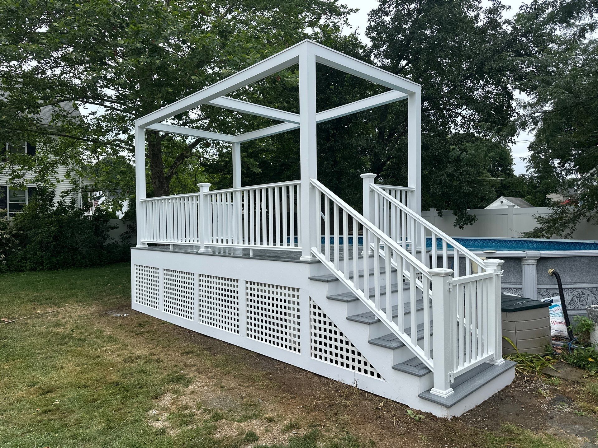After build: custom white pergola poolside deck with grey composite decking, enclosed square lattice panels, and gate