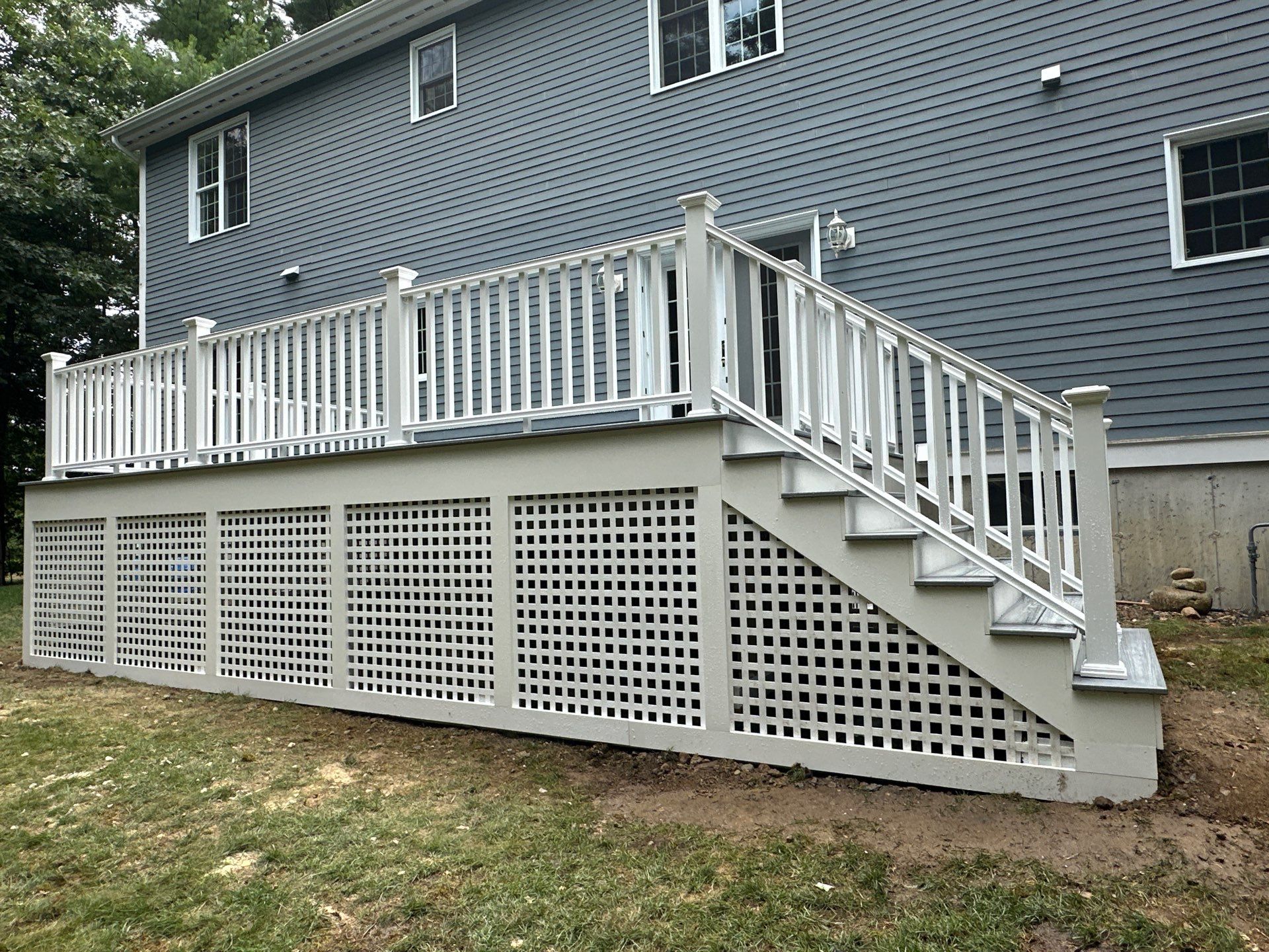 Side elevation of completed raised backyard deck with white vinyl railings, staircase, and full square lattice skirt panels