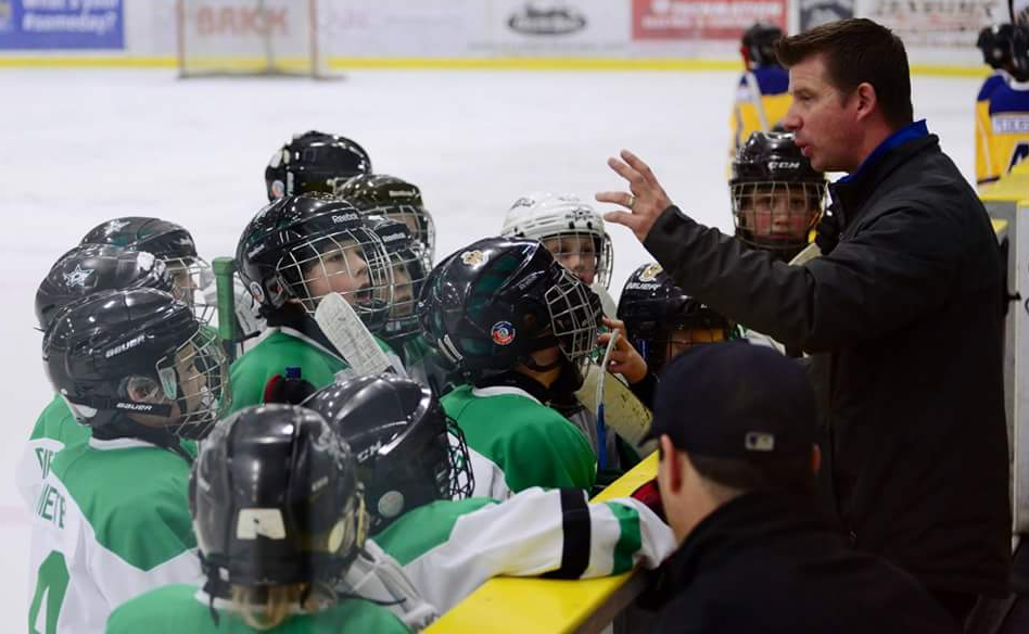 Larry Moberg giving instructions to young hockey players at the bench.