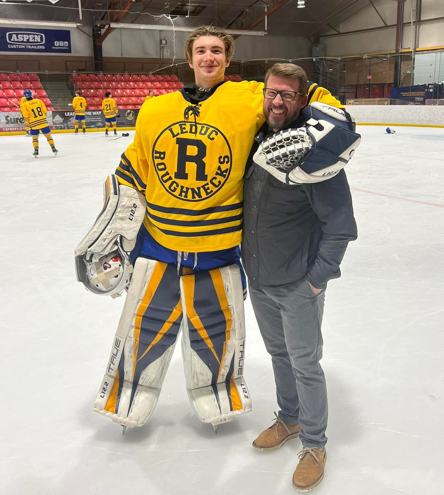 Larry Moberg and Kael smiling together at a hockey rink.