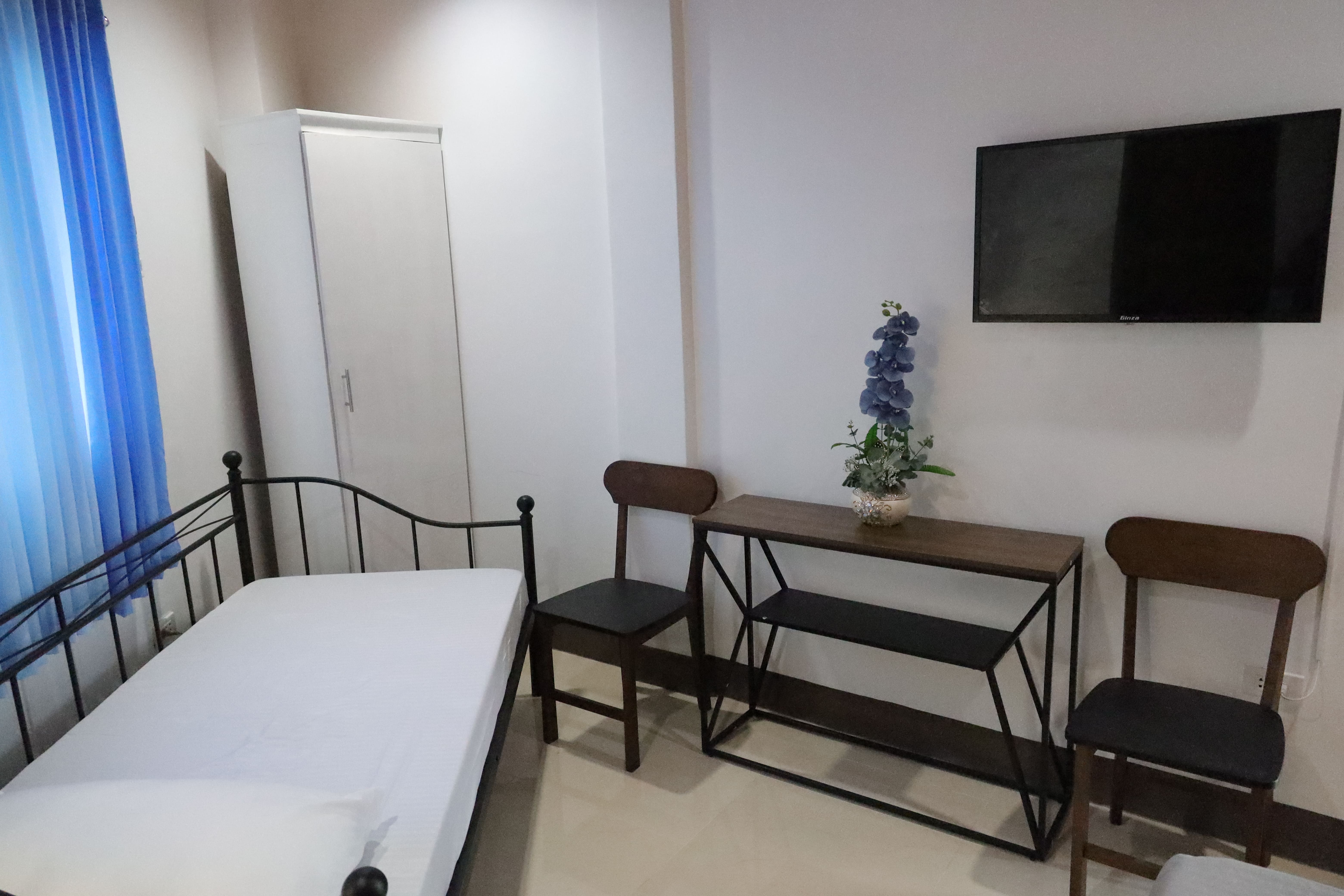 Room interior showing work desk, chairs, wardrobe, wall-mounted Smart TV, and floral accent