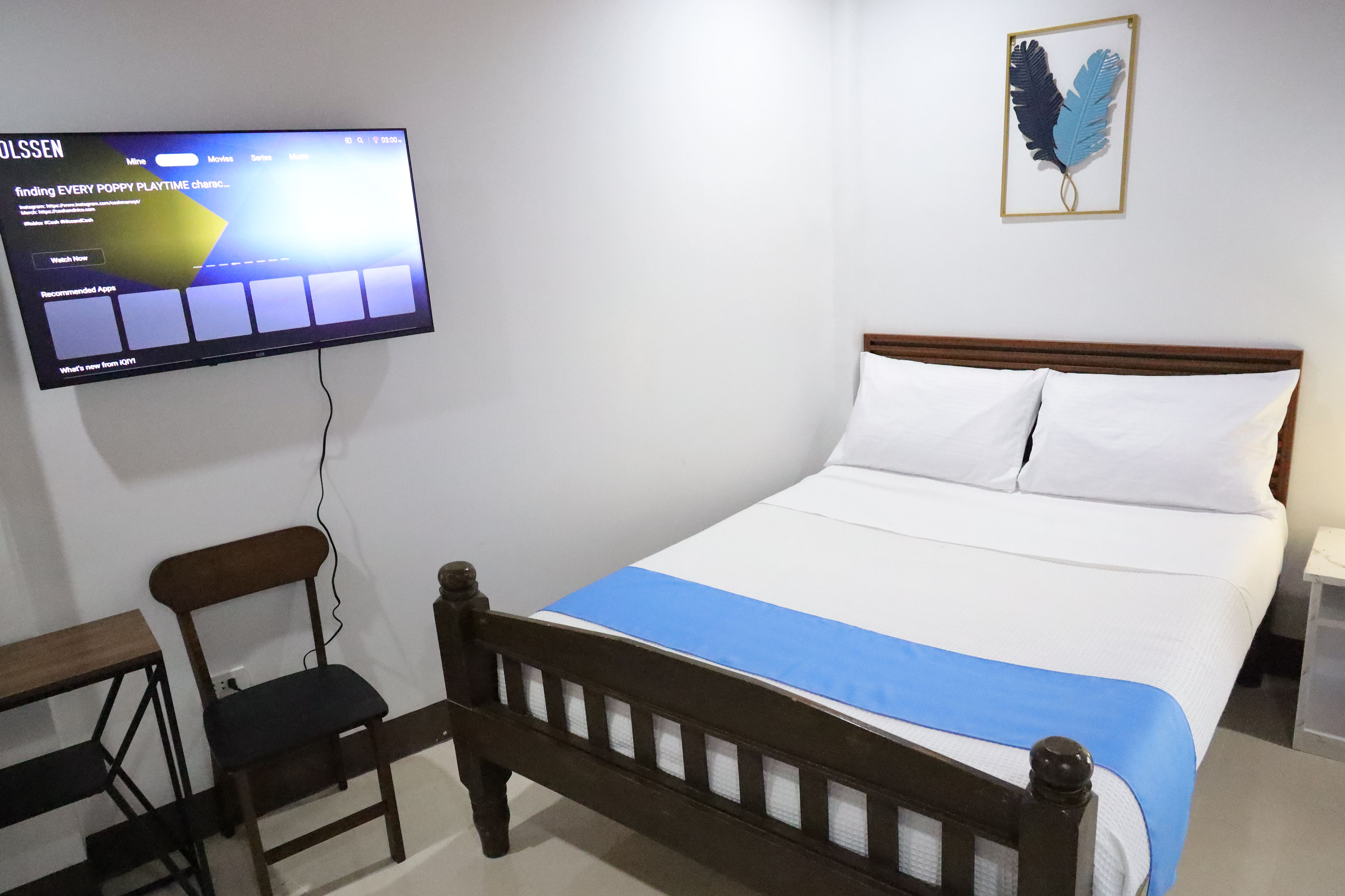 Guest bedroom with large wall-mounted Smart TV and comfortable wood-framed bed
