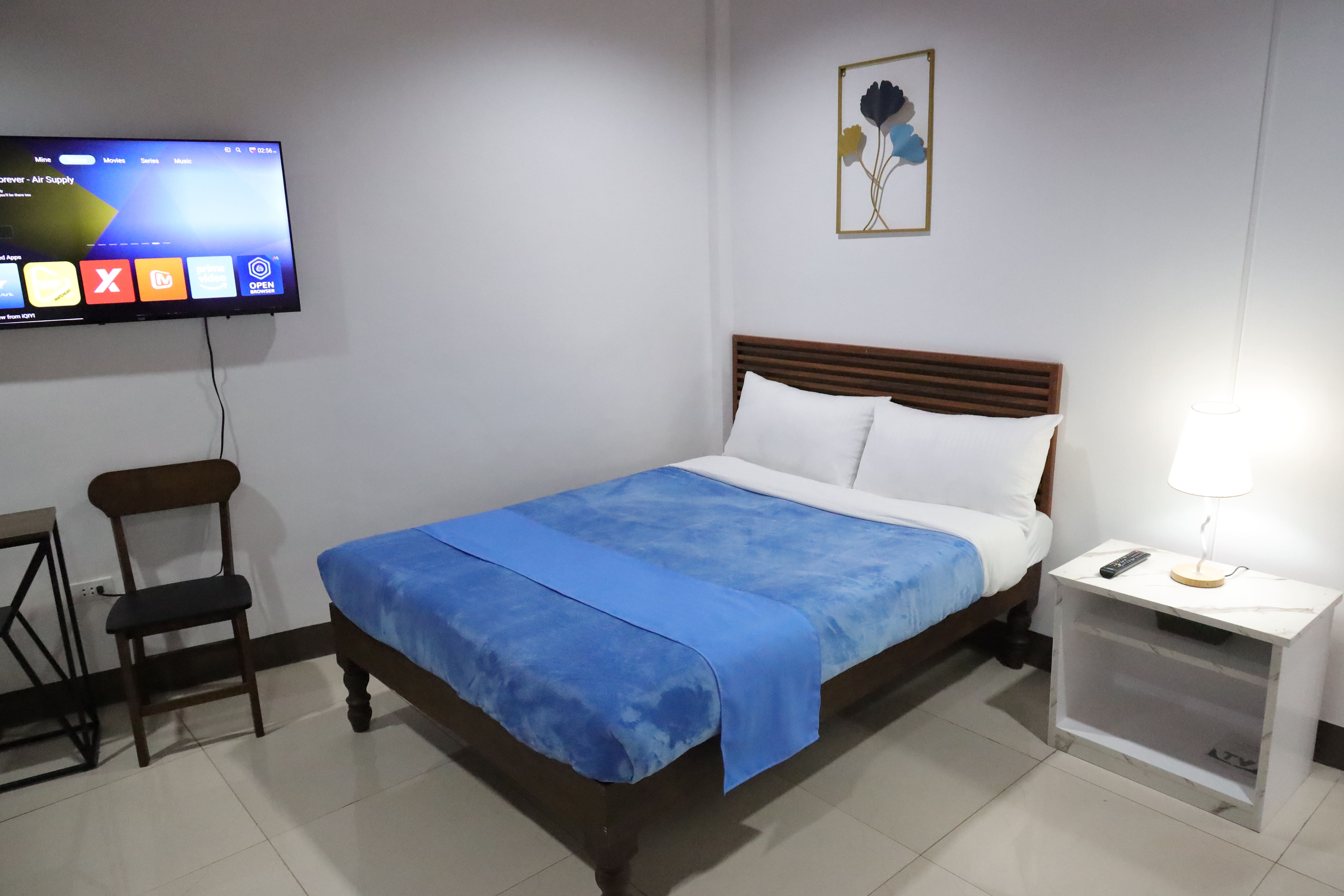 Wood-framed bed with blue plush duvet, bedside lamp, marble nightstand, and wall art