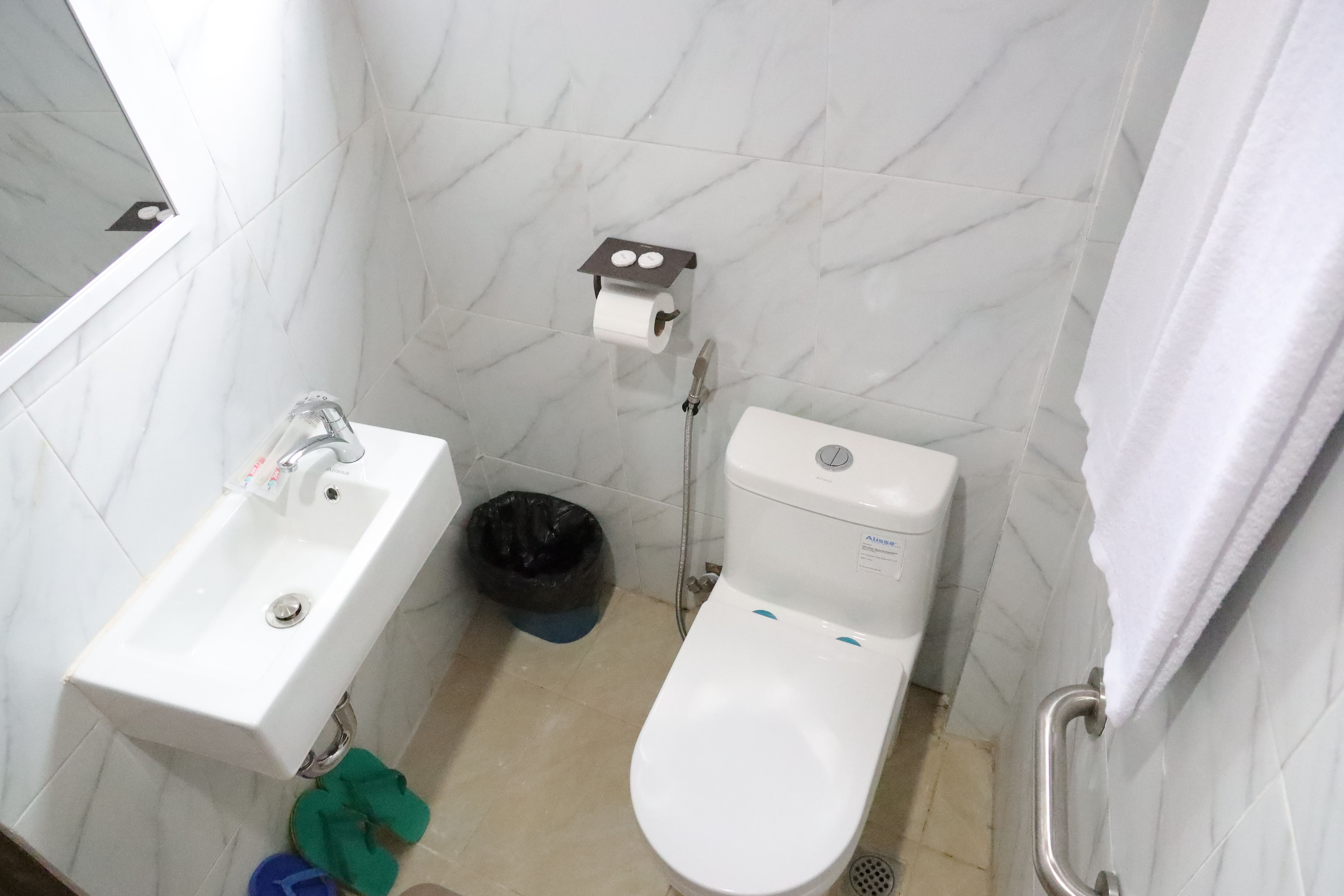 Clean private bathroom with marble-style tiles, modern toilet, bidet spray, sink, and fresh towels