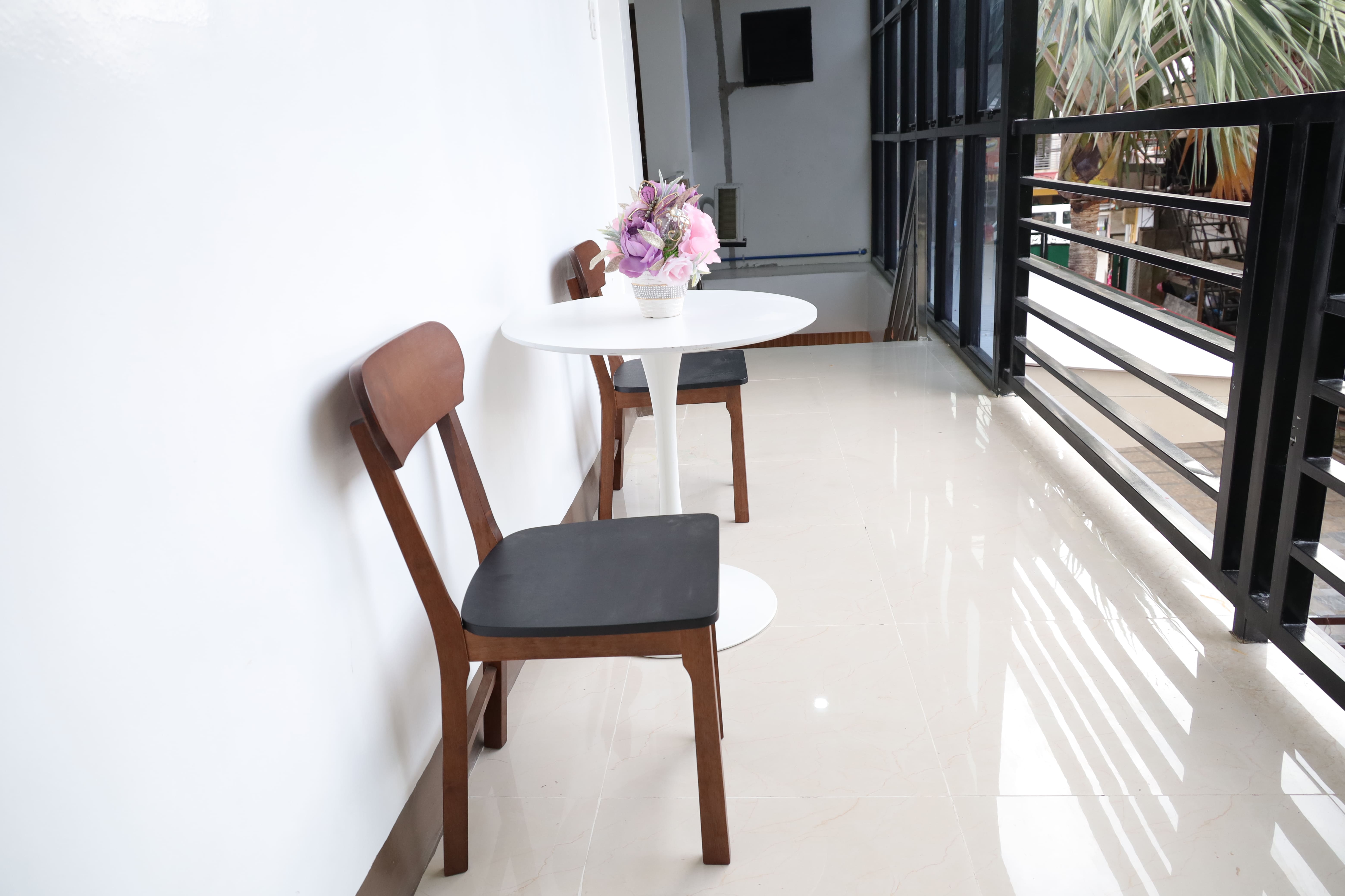 Bright corridor seating with wood chairs, round white table, and black metal railings
