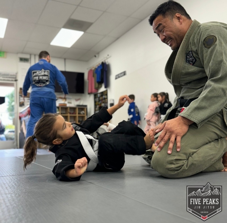 Five Peaks coach mentoring and smiling with a young kids jiu jitsu student practicing technique on the mat