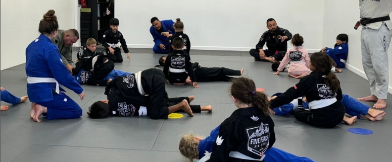 Kids and coaches training techniques on the mats at Five Peaks Jiu Jitsu