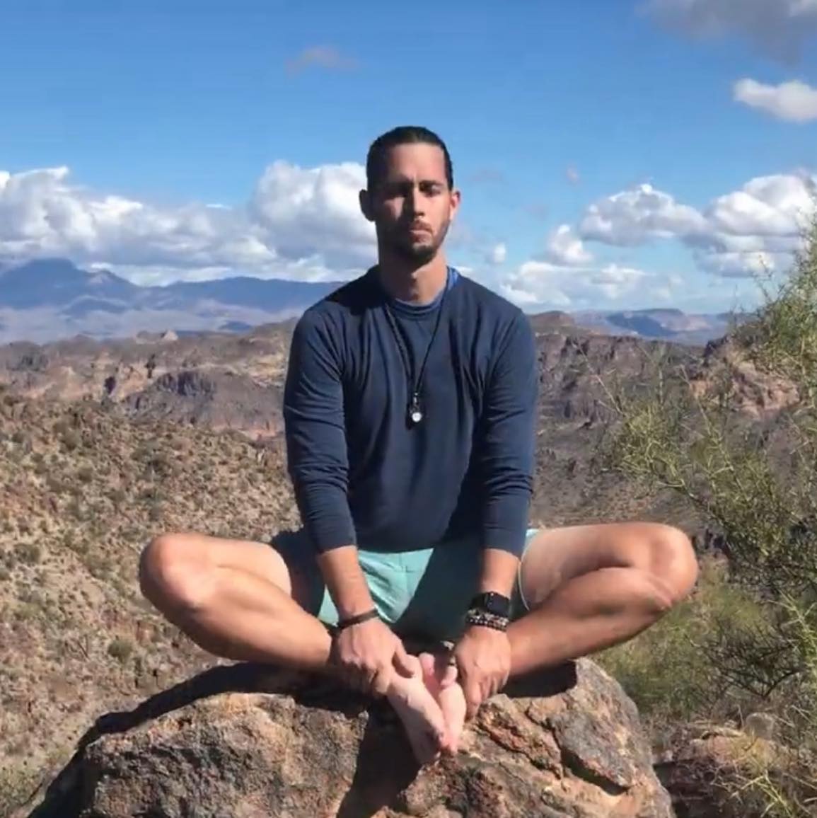 Christopher Hanson seated in stillness on a high summit vantage, watching the horizon.