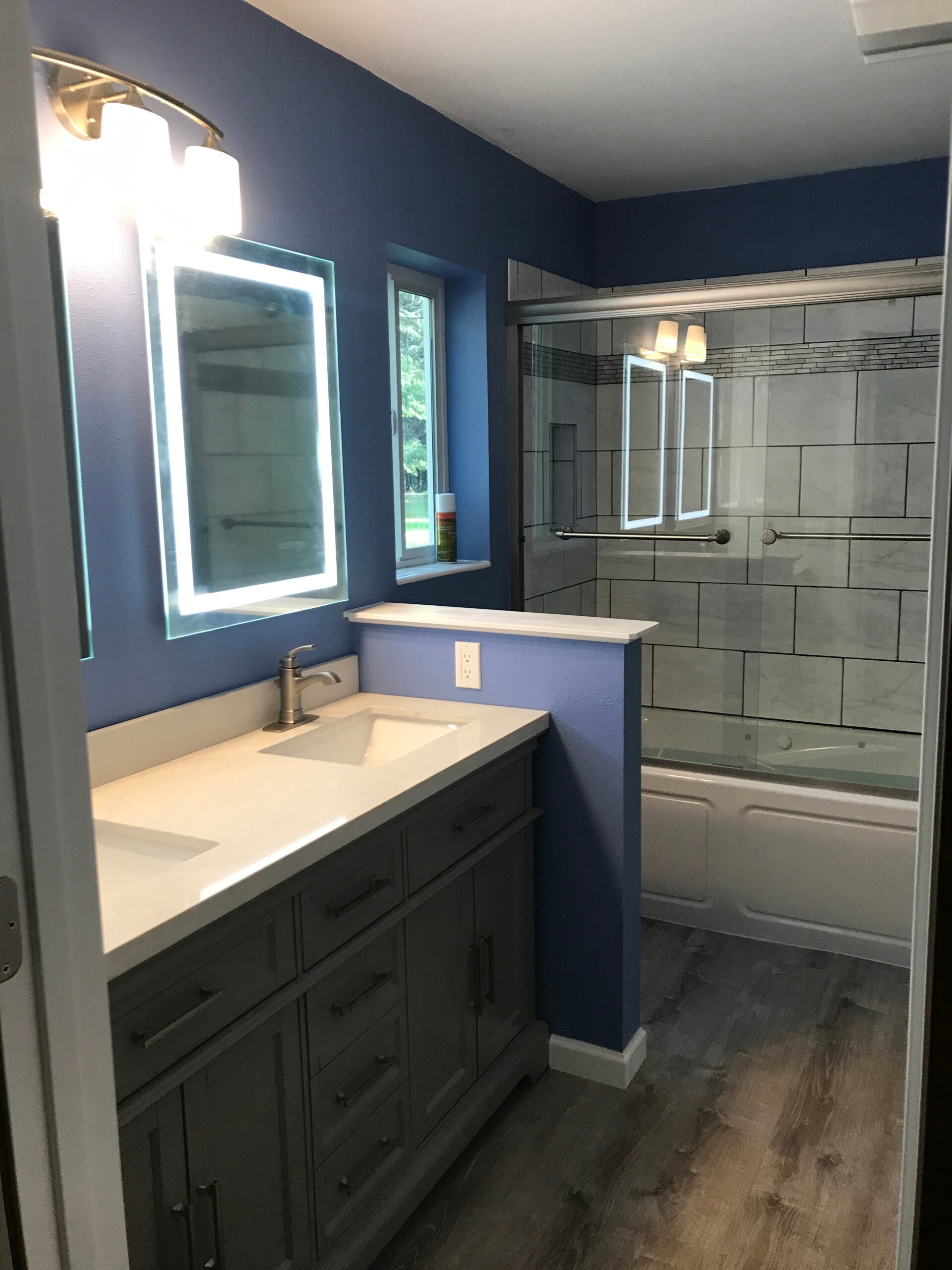 Remodeled bathroom with double vanity, lighted mirror and tiled tub surround by Bruin Builders