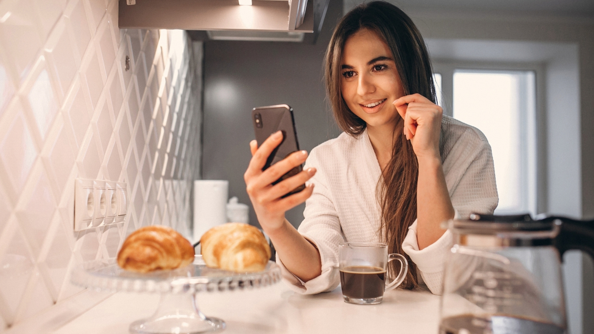 Business owner smiling at a message on her phone over morning coffee at home