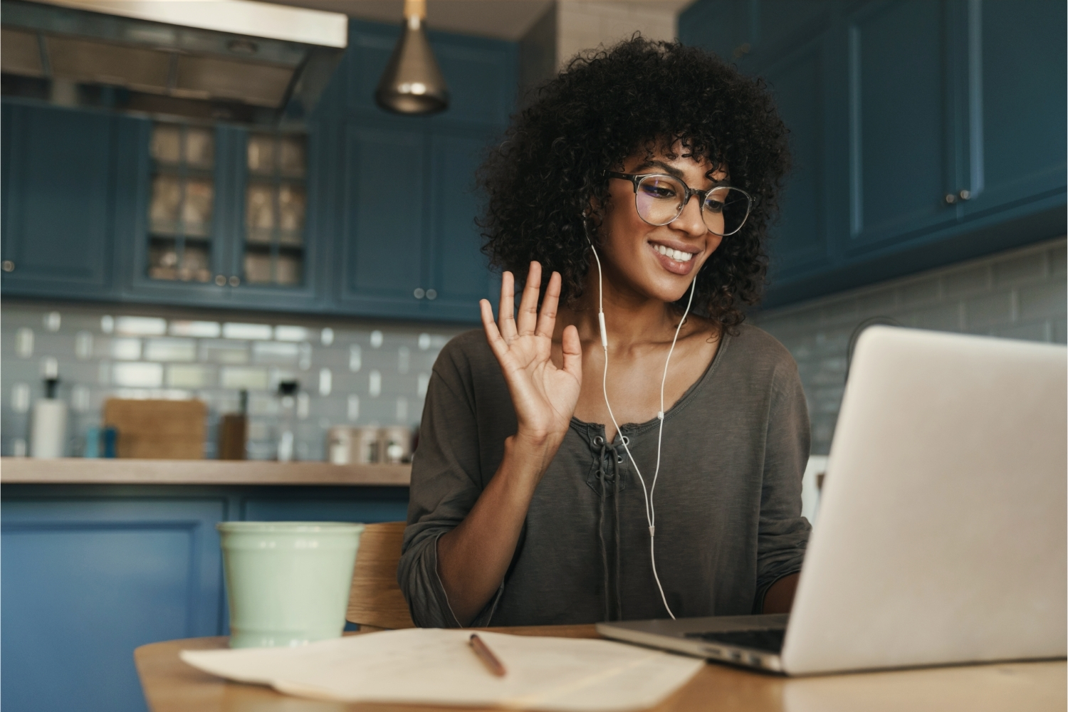 Business owner waving hello on a relaxed video call from her kitchen