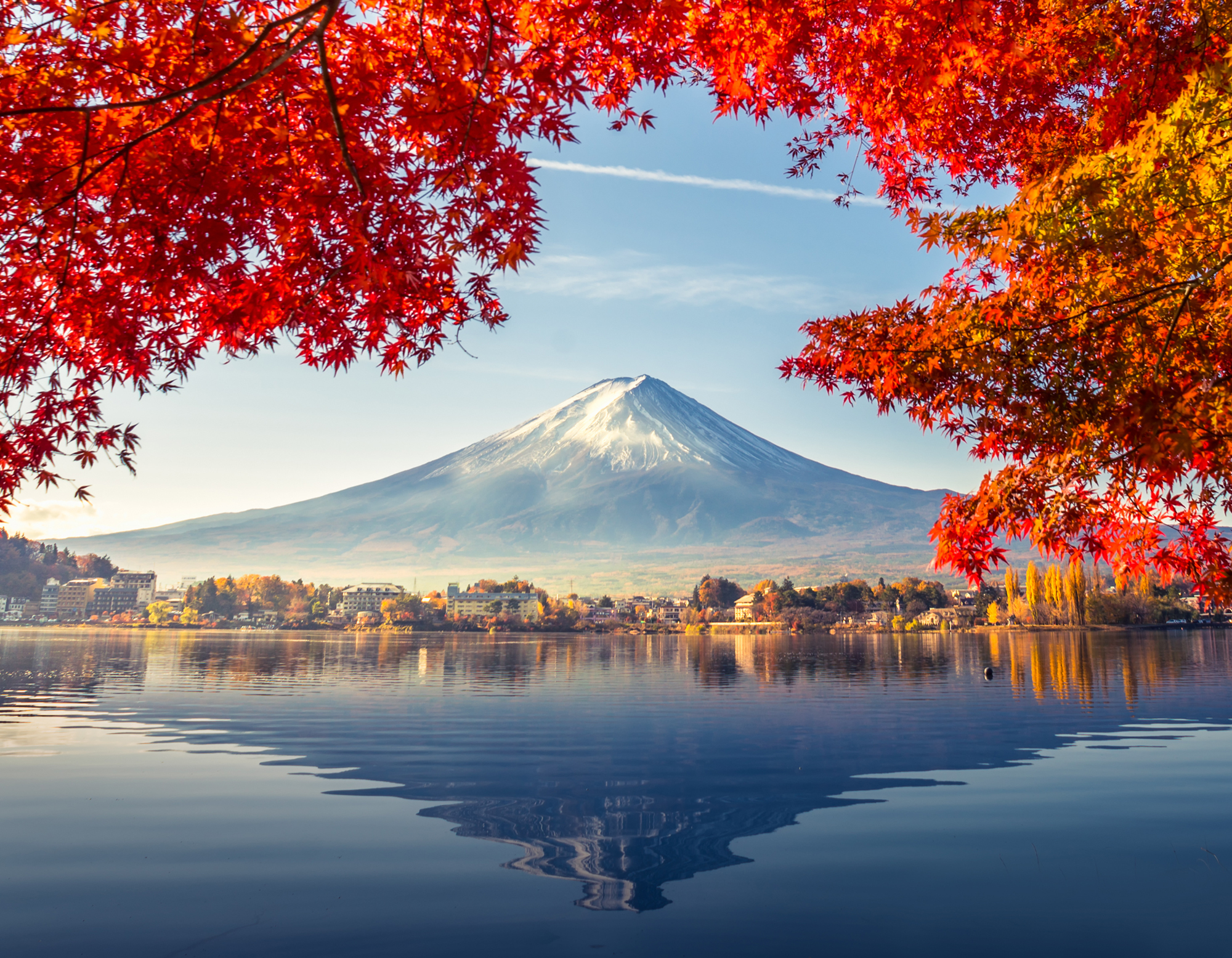 Mount Fuji reflected across the water framed by vibrant red autumn leaves