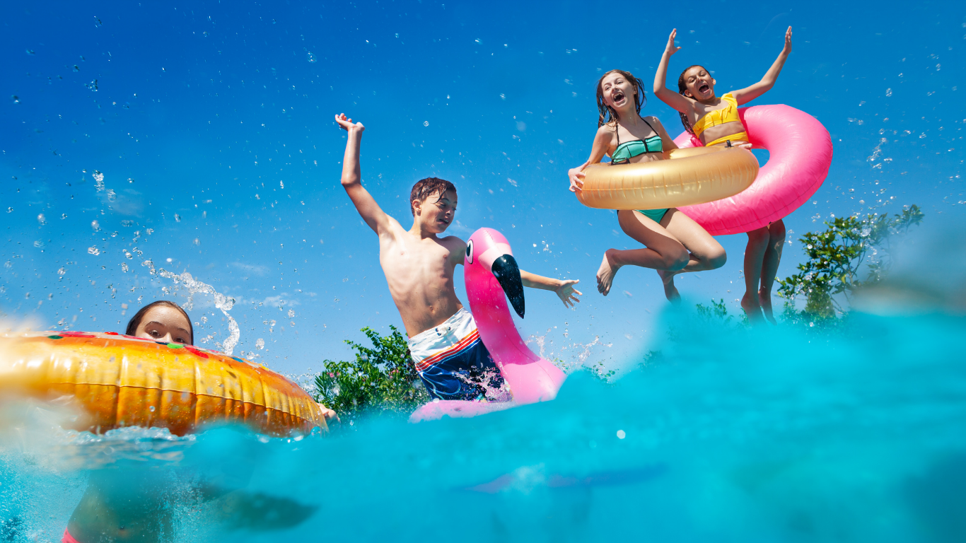 Kids joyfully jumping into a crystal clear pool with colorful floats under a bright blue summer sky
