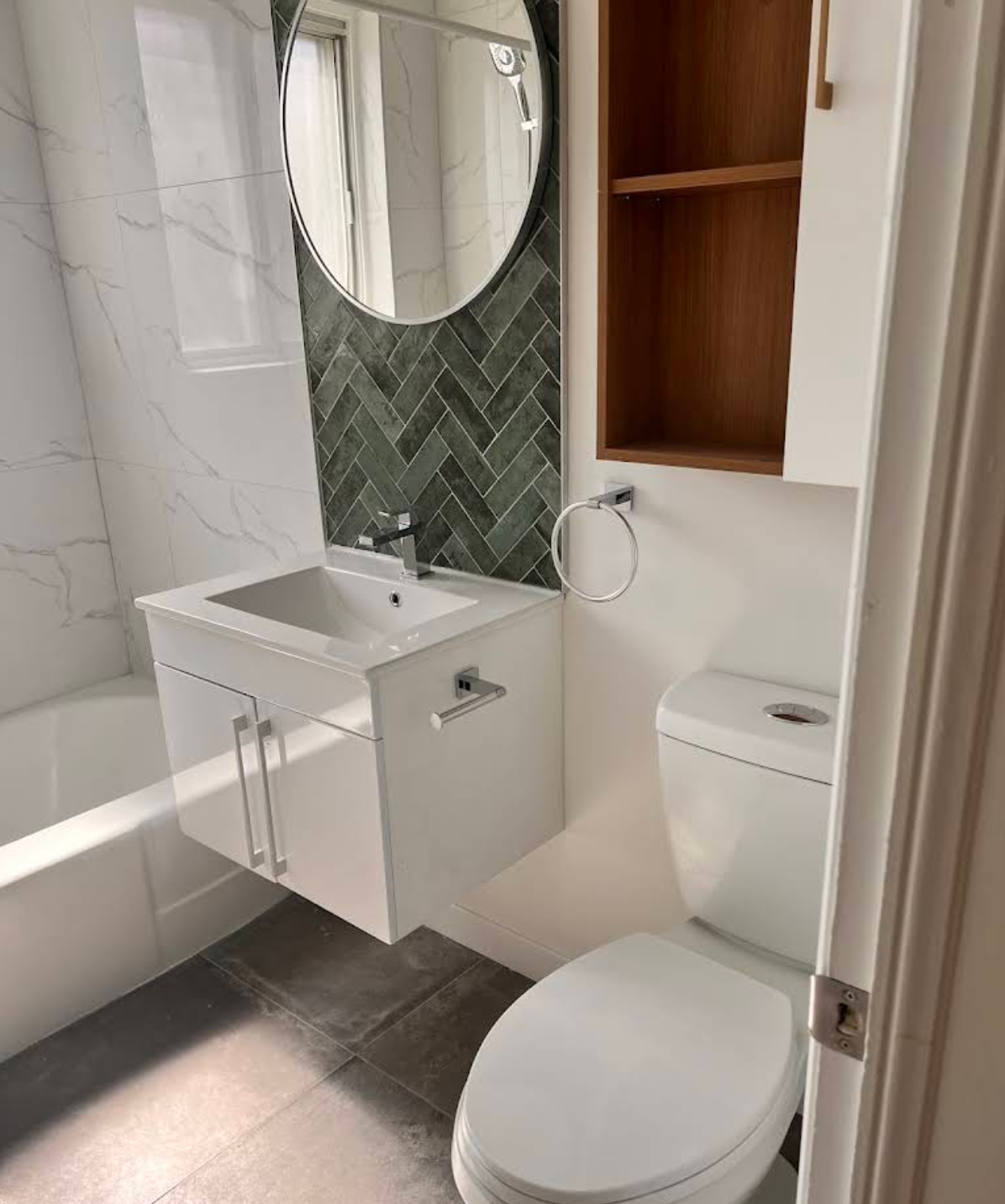 Rénovation de salle de bain complète — vanité suspendue, miroir rond et faïence chevrons vert forêt