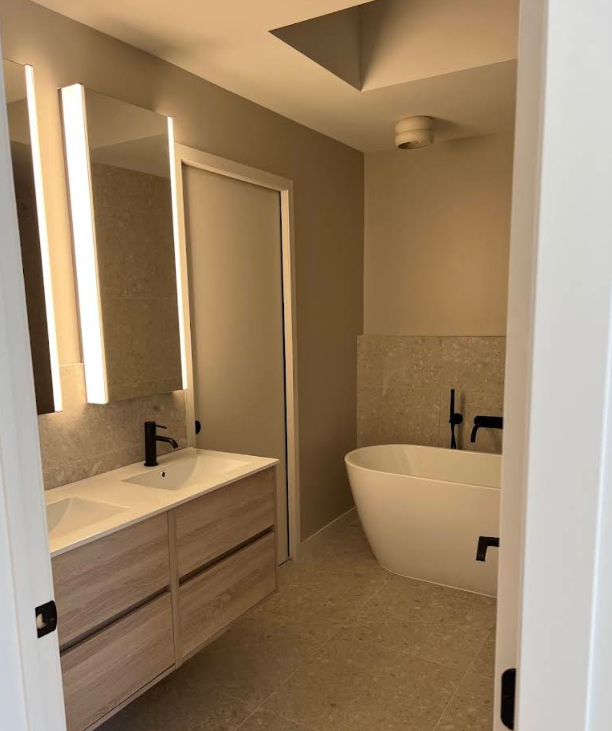 Salle de bain moderne complète avec meuble double vasque suspendu bois, miroirs rétroéclairés LED verticaux et baignoire îlot autoportante avec robinetterie noire mate encastrée