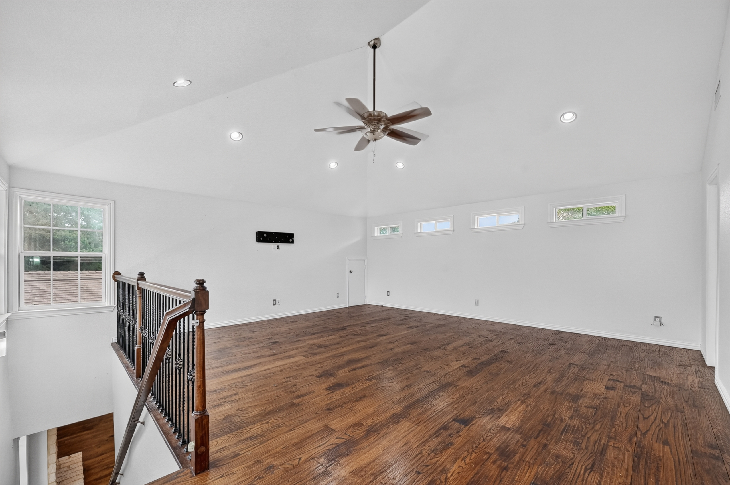 Upstairs open game room and loft living space with hardwood floors, wrought iron railing, and vaulted ceilings