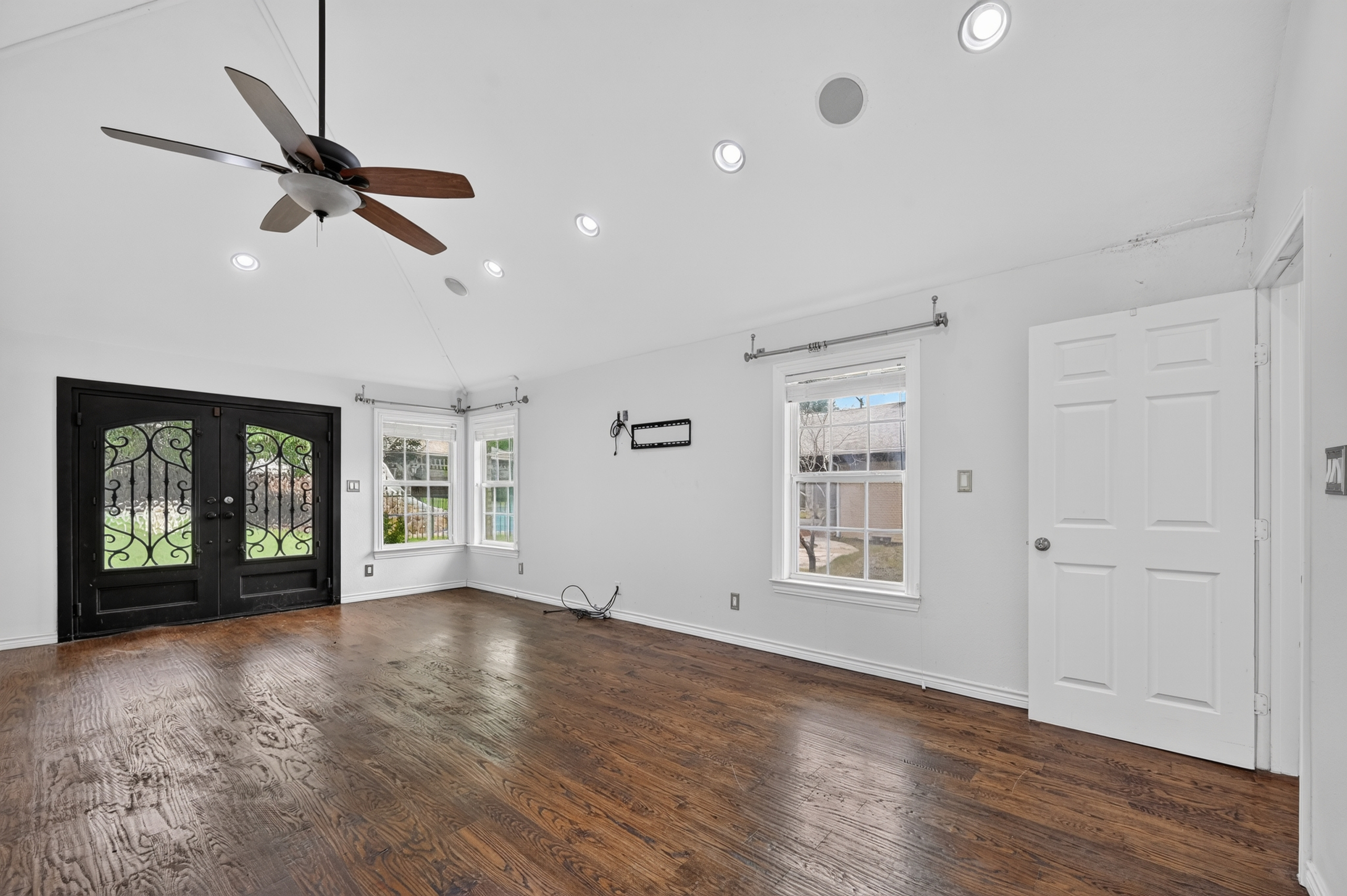 Sunlit living space with vaulted high ceiling, recessed architectural lighting, and iron French doors