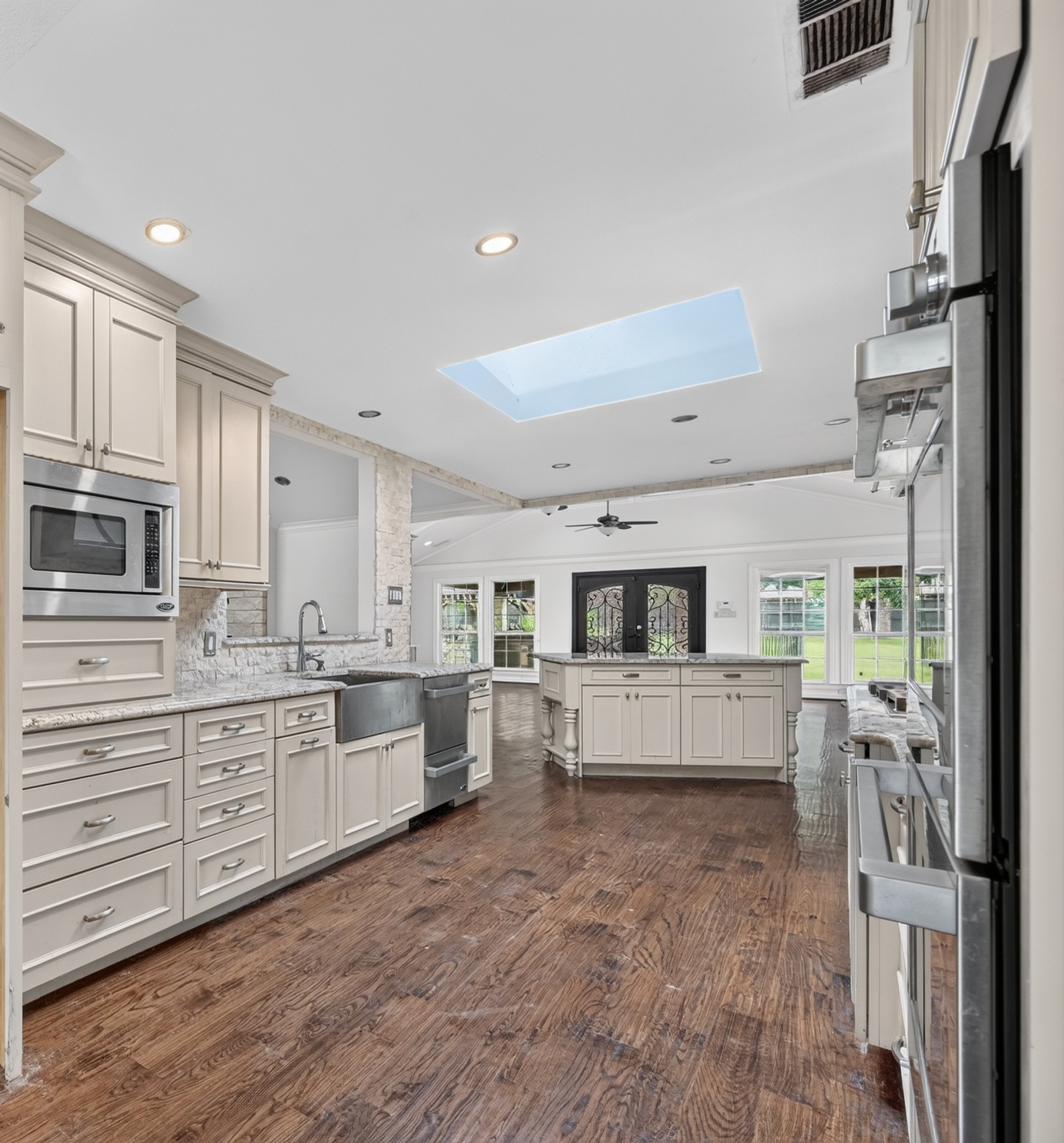 Gourmet chef's kitchen featuring custom cabinetry, skylight, granite countertops, prep island, and hardwood floors