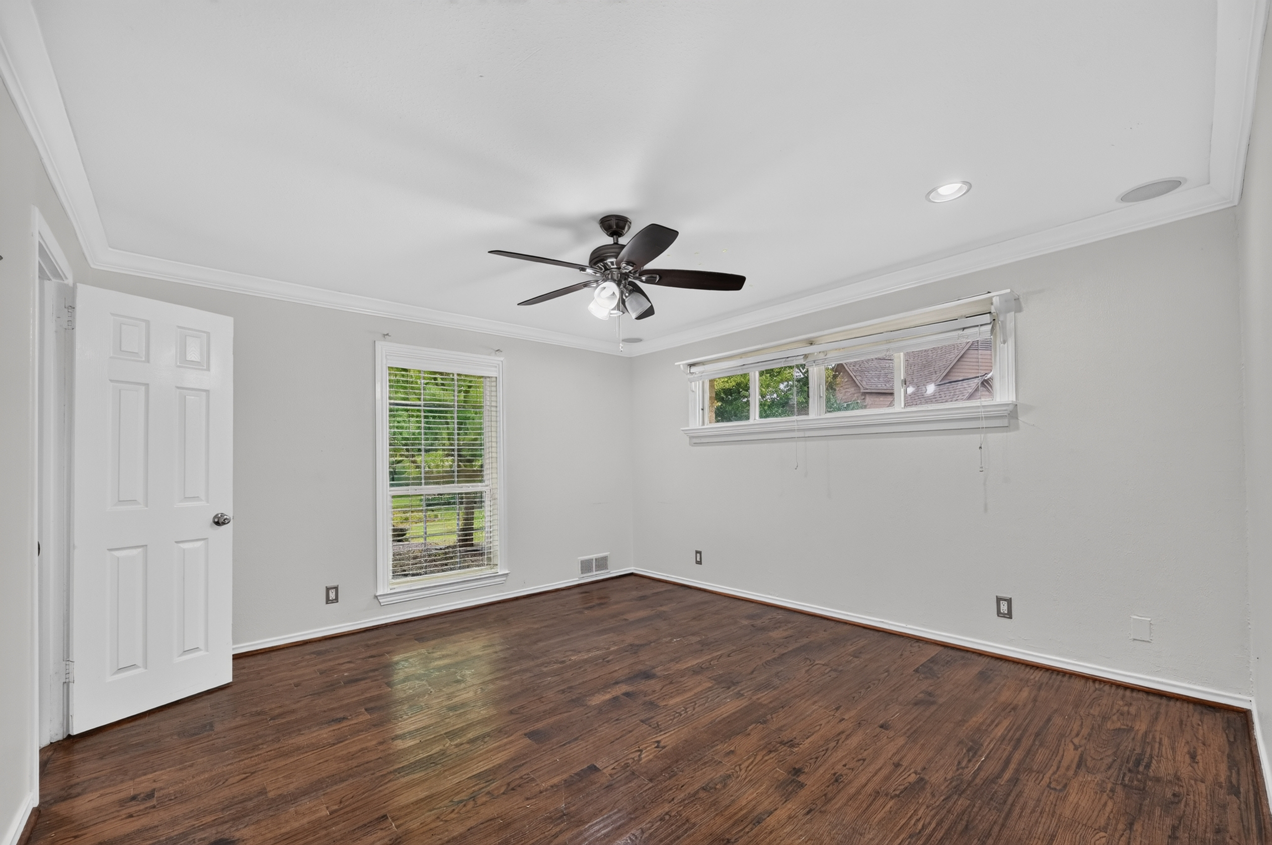 Spacious private bedroom with rich hardwood floors, designer ceiling fan, and crown molding