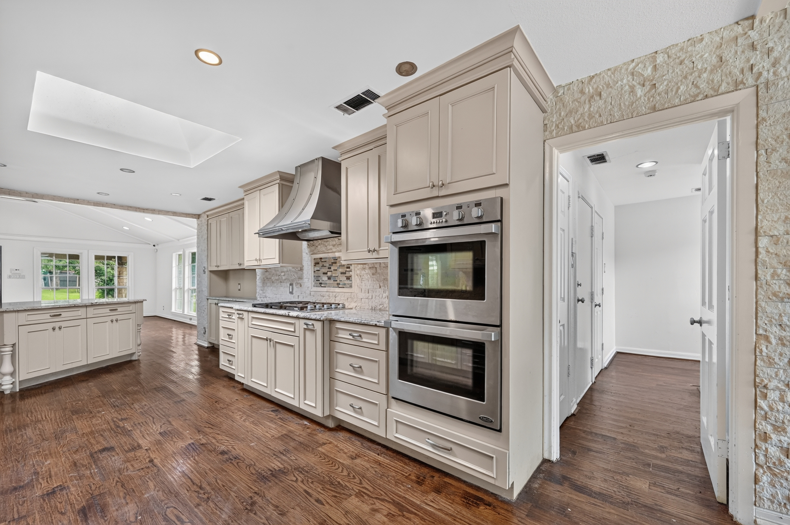 Gourmet chef's kitchen with commercial stainless vent hood, double wall ovens, stone accent walls, center prep island, and skylight