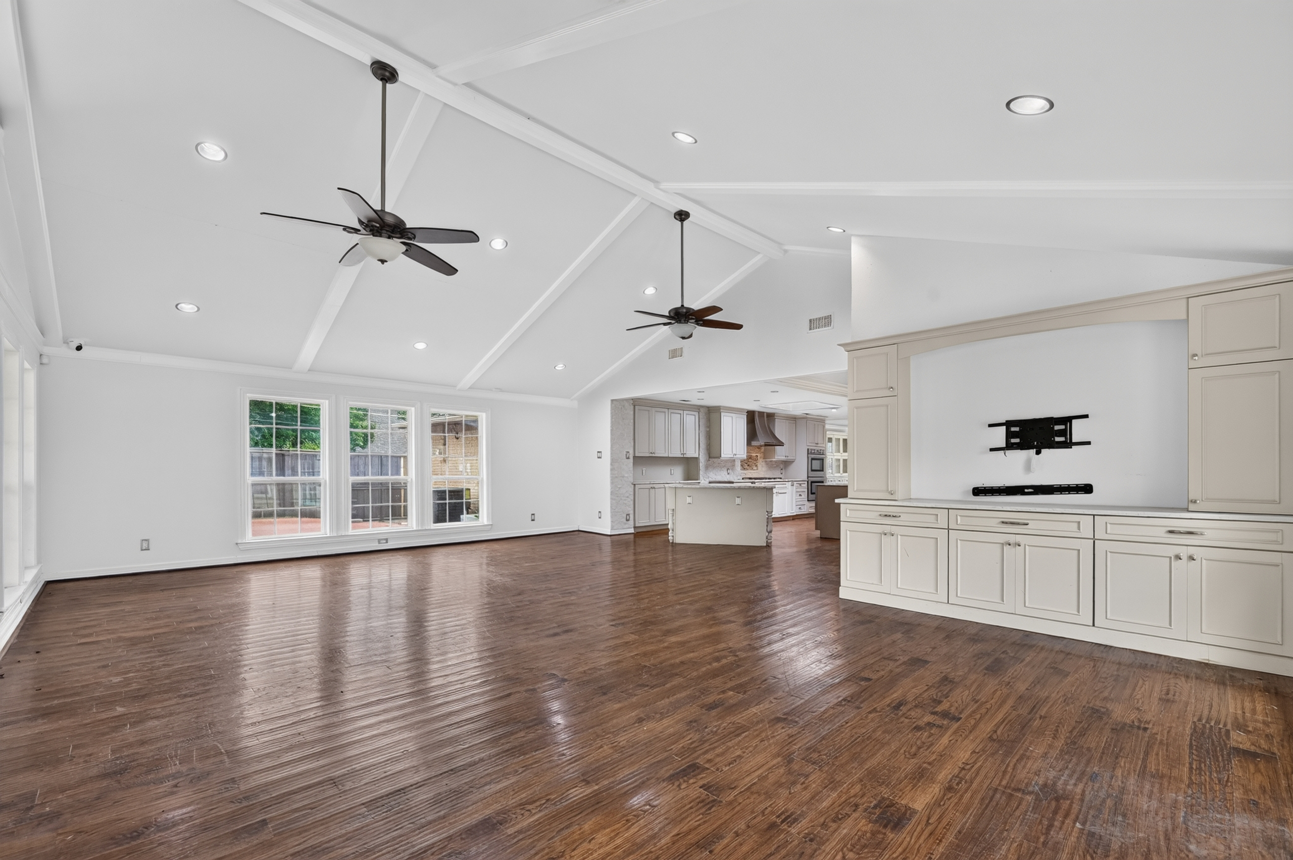 Vaulted great room featuring built-in entertainment credenza, architectural ceiling beams, dual ceiling fans, and window wall
