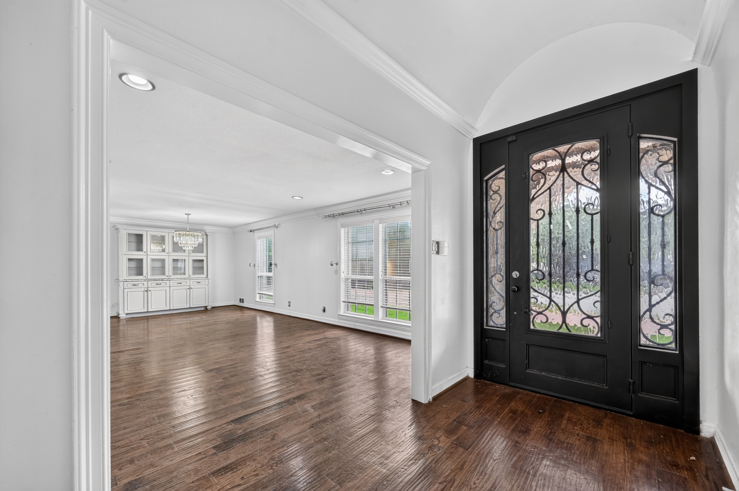 Grand arched foyer with custom wrought-iron front door, hardwood floors, and view into the formal dining room with built-in buffet