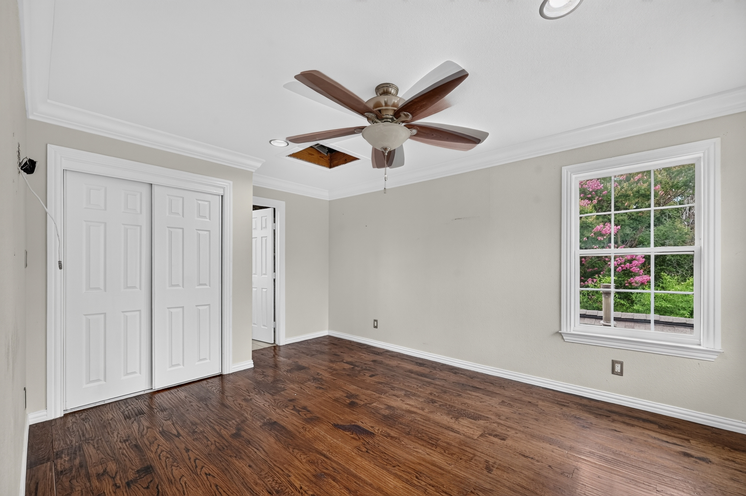 Guest bedroom with double panel closet doors, crown molding, ceiling fan, and tree-lined window view