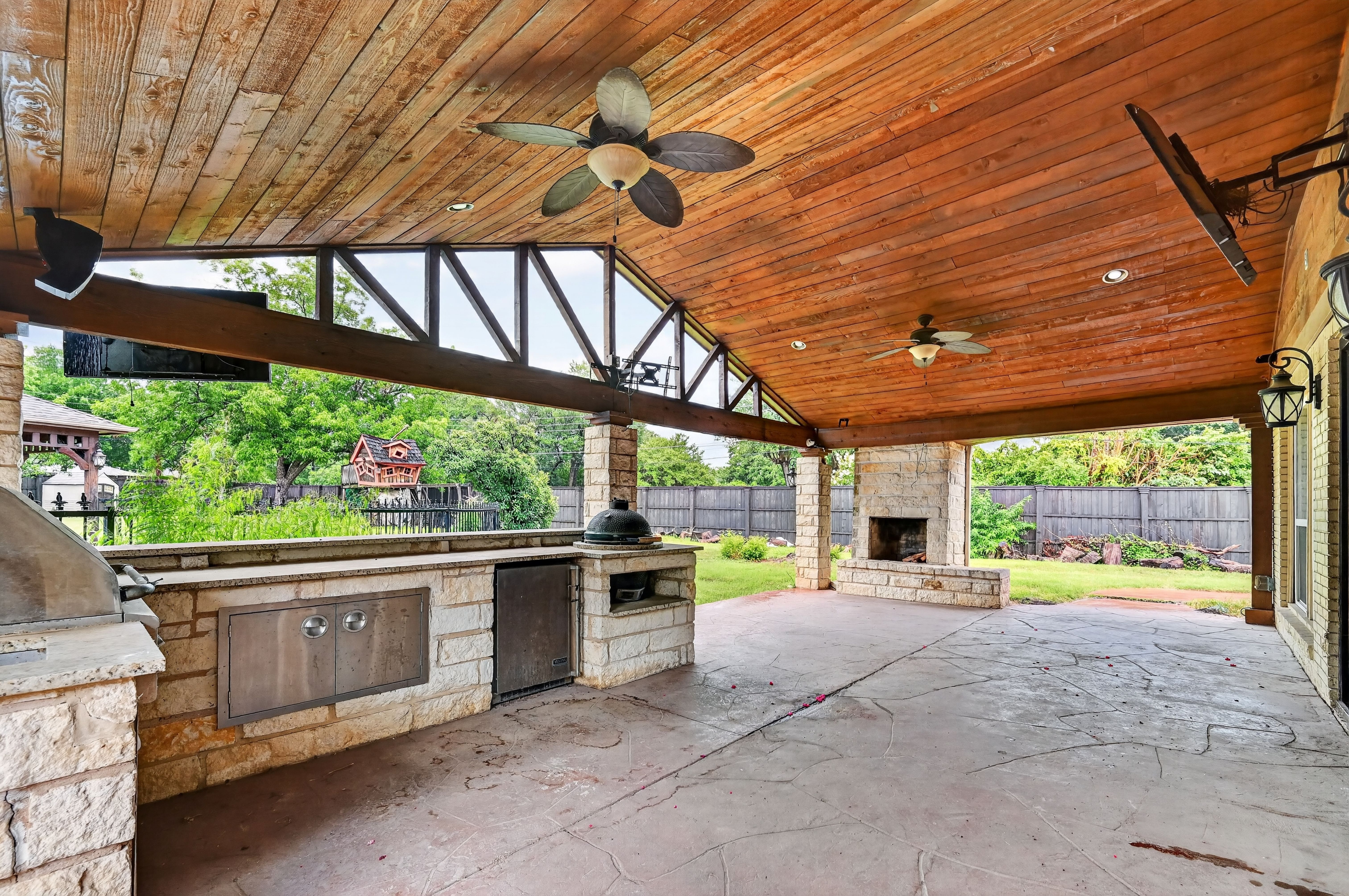 Spacious outdoor cedar pavilion with outdoor summer kitchen, built-in BBQ grill, stone fireplace, ceiling fans, and stamped concrete patio