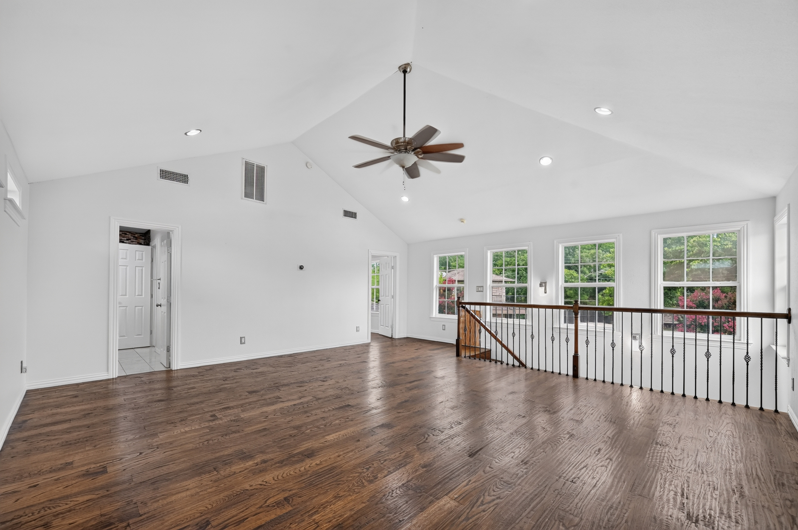 Sunlit upper entertainment gallery with tree canopy window vistas, custom wrought iron balustrade, and vaulted ceilings