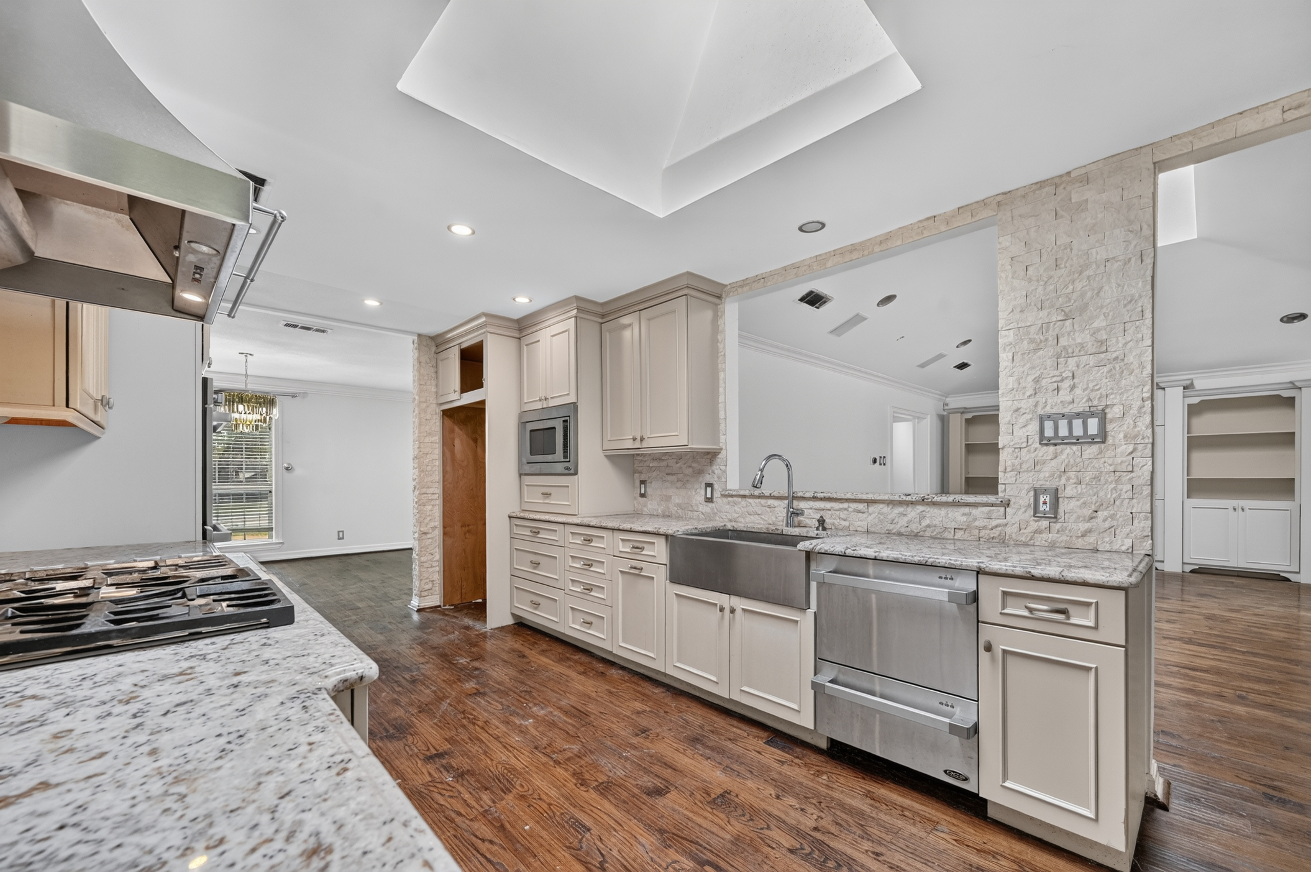 Chef's kitchen featuring stainless farmhouse sink, dual-drawer dishwasher, stone-trimmed pass-through bar, skylight, and gas cooktop