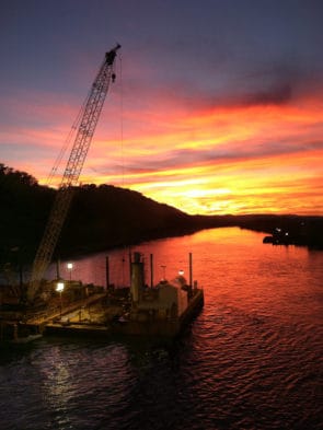 Barcaza de construcción marina con grúa trabajando en aguas fluviales al atardecer
