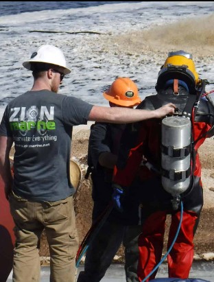 Buzo comercial preparándose con traje sellado para inmersión en agua contaminada en planta de tratamiento de aguas residuales
