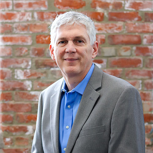Professional business headshot against a brick wall
