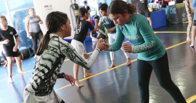 Two young 10th Planet Torrance grapplers in rash guards slapping hands and locking into stance on the mat