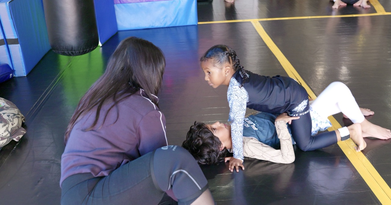 Coach guiding young Little's JJ student in mount control and eye contact on the mat
