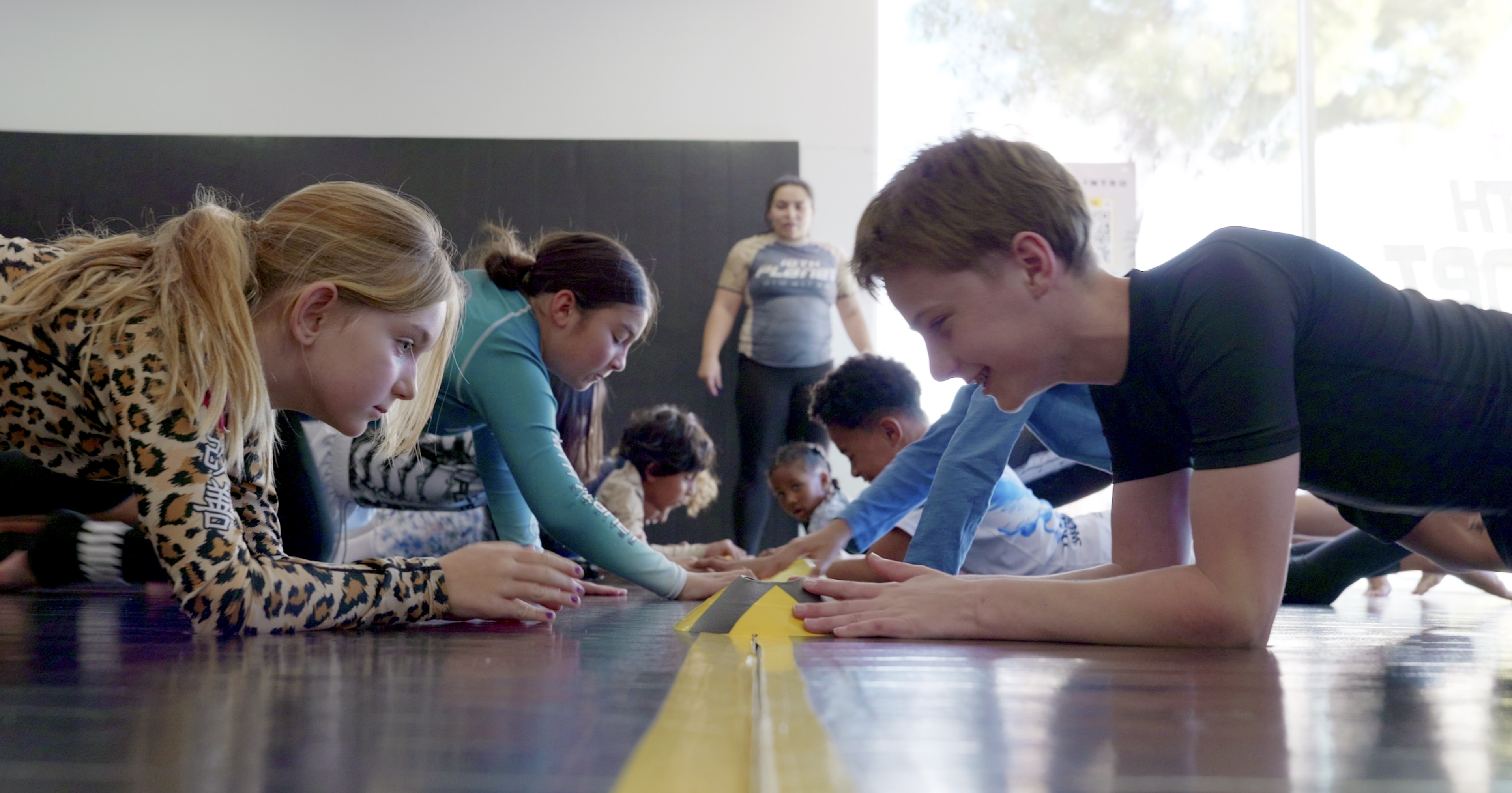 Students laughing during a cone reaction plank game on the mat with Coach