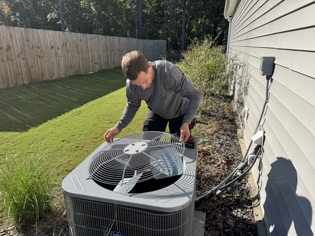 Mike Abbott inspecting the fan assembly of an outdoor Carrier air conditioning unit during residential HVAC maintenance in Aberdeen, NC.