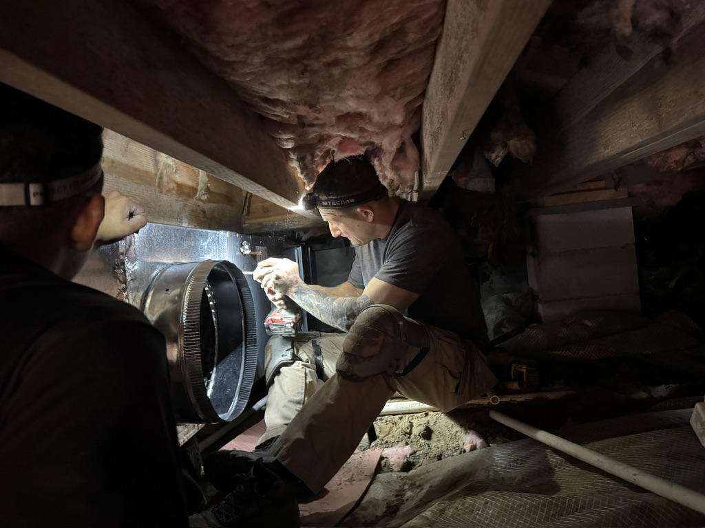 Mike Abbott installing sheet metal ductwork connections in a residential crawl space in Seven Lakes, NC