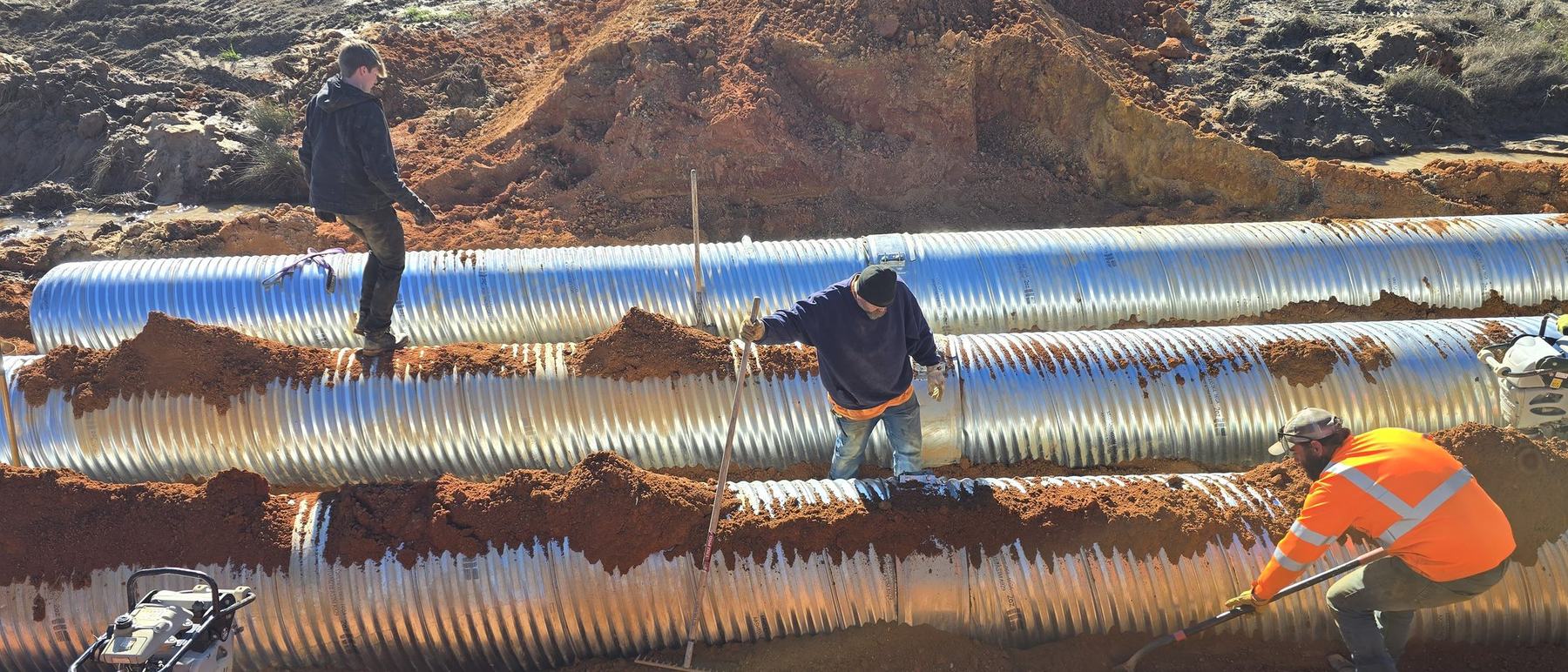 Three JT Lee crew members in high-visibility gear setting large storm drain pipe