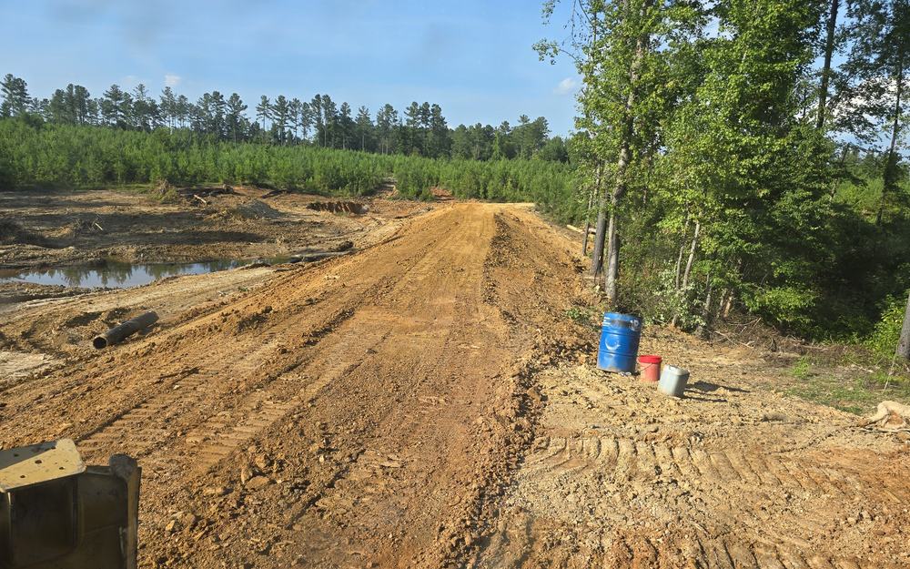 A graded earth embankment and re-established roadbed through cleared ground