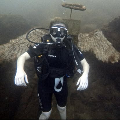 Diver floating in front of submerged stone angel wings and halo