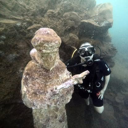 Diver swimming close to a submerged statue in Lake Ilopango