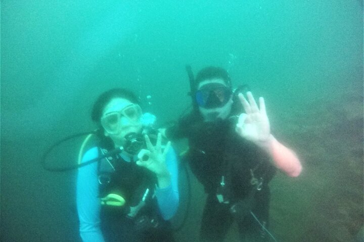Two divers giving the OK sign in the green volcanic water of Lake Ilopango