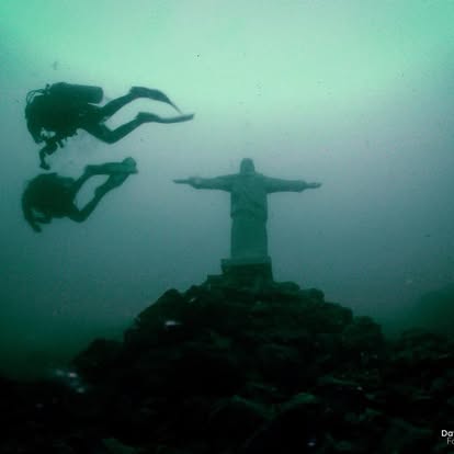 Divers descending toward the submerged Christ statue in Lake Ilopango