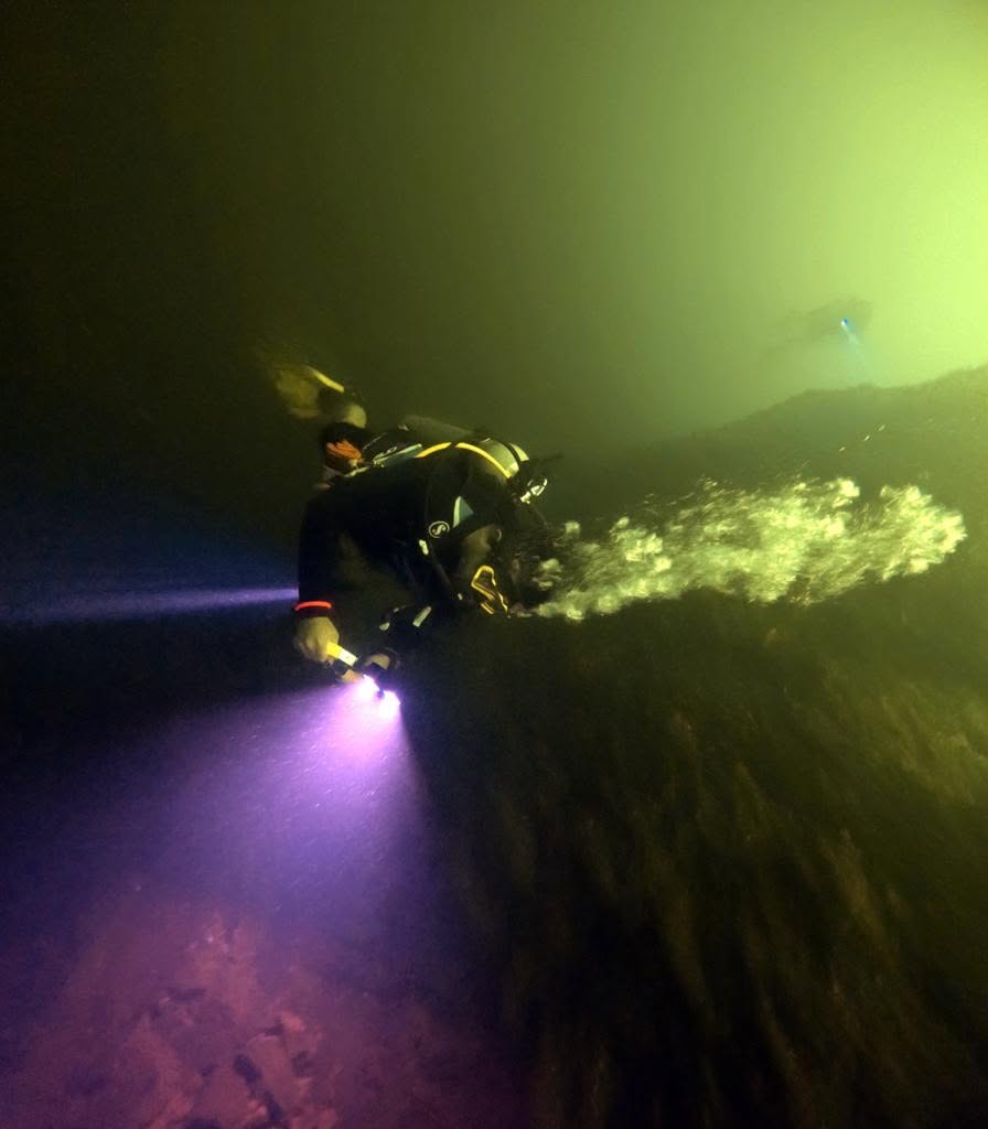 Diver exploring steep volcanic rock drop-off with a dive light