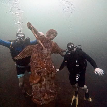 Two divers alongside submerged winged angel statue in Lake Ilopango