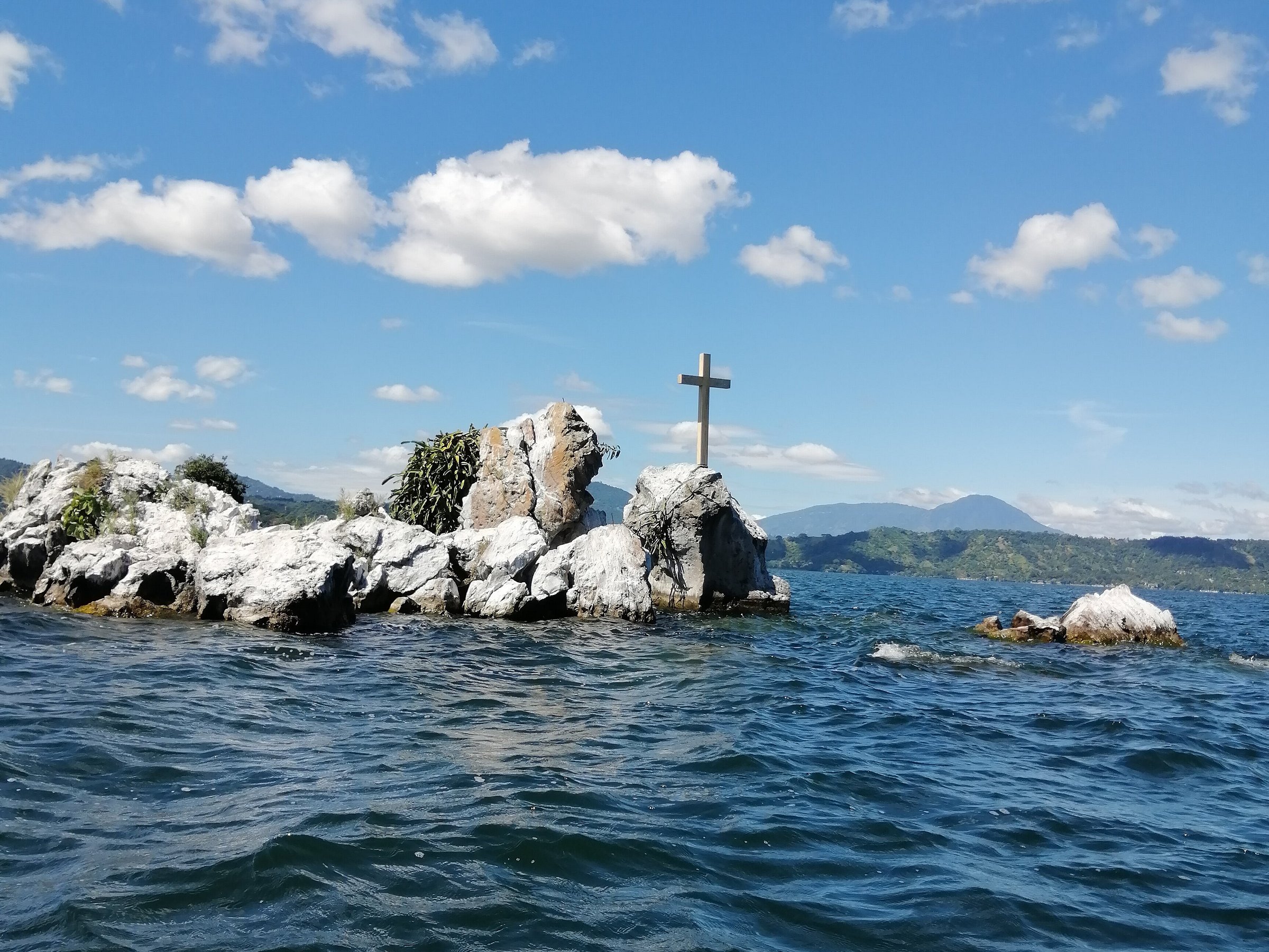 Rocky island outcrop with a cross against the blue sky at Lake Ilopango