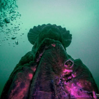 Upward view of submerged statue with bubbles rising in Lake Ilopango