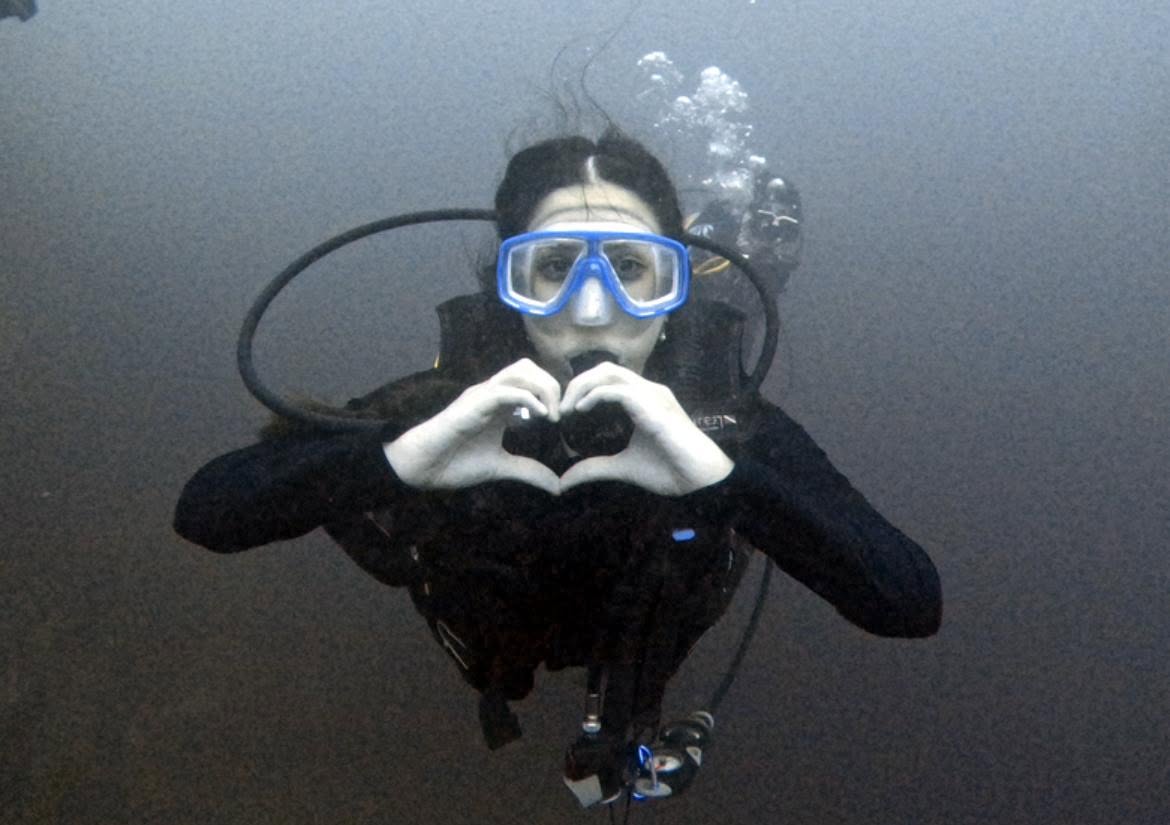 Diver making a heart gesture with hands underwater in Lake Ilopango